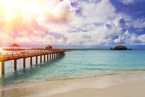 Maldivas. O mar azul-turquesa ao sol e a ponte de madeira sobre a água
 - Foto, Imagem