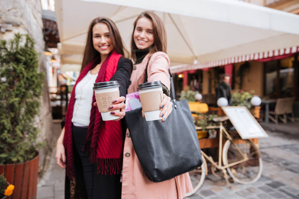 Two smiling attractive young women holding cups of takeaway coffee - Foto, Imagem