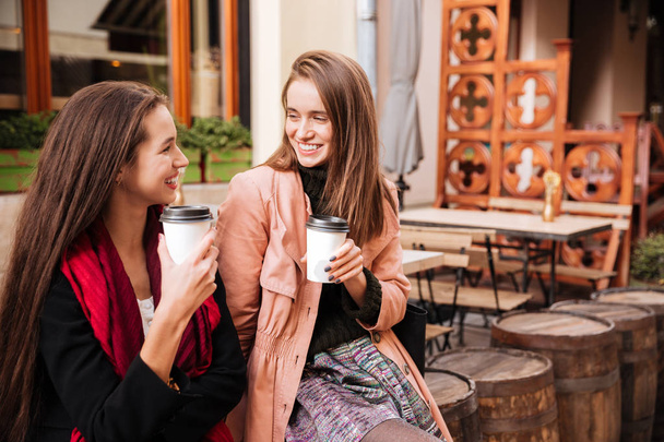 Two cheerful women talking and drinking coffee in old city - Fotoğraf, Görsel