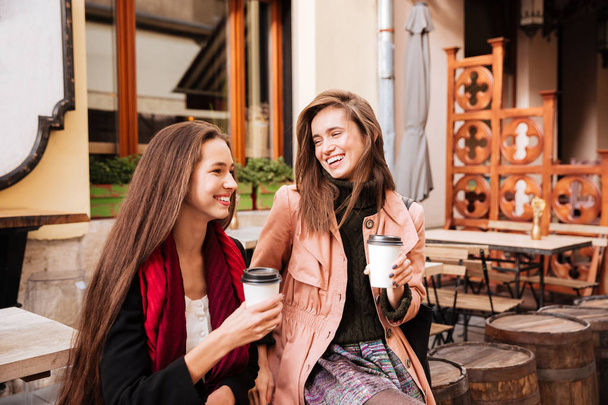 Two cheerful women with cups of coffee talking and laughing - Foto, imagen