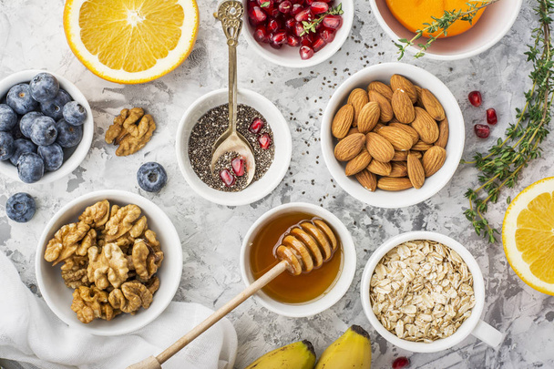 Ingredients for a healthy breakfast, nuts, oatmeal, honey, berries, fruits, blueberry, orange, pomegranate seeds, almonds, walnuts The concept of natural organic food in season Top - Фото, изображение