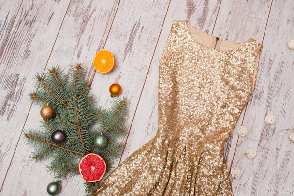 Золотое платье с блестками на деревянном фоне, еловая ветвь и шары и цитрусовые
 - Фото, изображение