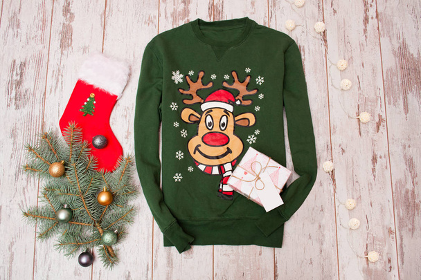 Zelený svetr s jelenem na dřevěné pozadí. Vánoční větev s vánoční výzdobou, citrus, věnec, dárek - Fotografie, Obrázek