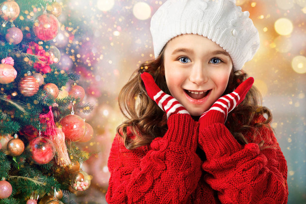Little girl in winter clothing surprised near Christmas tree - Foto, Imagen