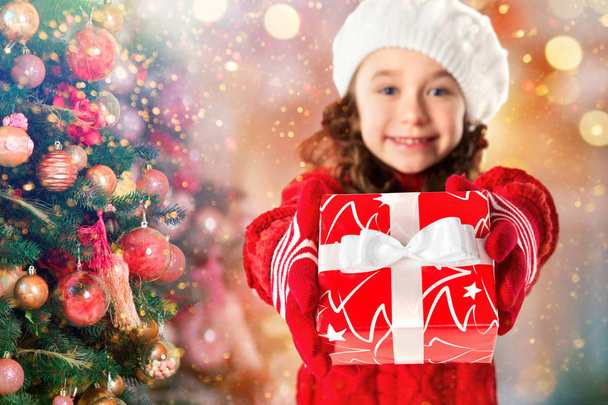 Счастливая маленькая девочка с подарком возле новогодней елки
 - Фото, изображение