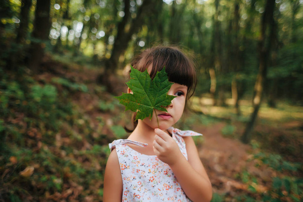 Mädchen, das im Wald steht und ein Blatt in der Hand hält. verstecktes b - Foto, Bild