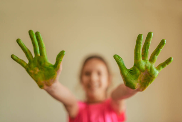 Pieni tyttö näyttää kädet, jotka maalattu vihreä maali
 - Valokuva, kuva