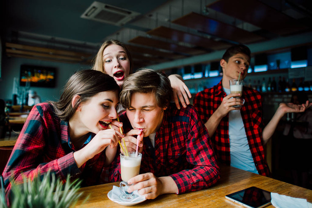 Un grupo de jóvenes amigos pasando el rato en una cafetería. Hombres y mujeres jóvenes que se reúnen en un café divirtiéndose y tomando café. Conceptos de estilo de vida, amistad y vida urbana
. - Foto, imagen