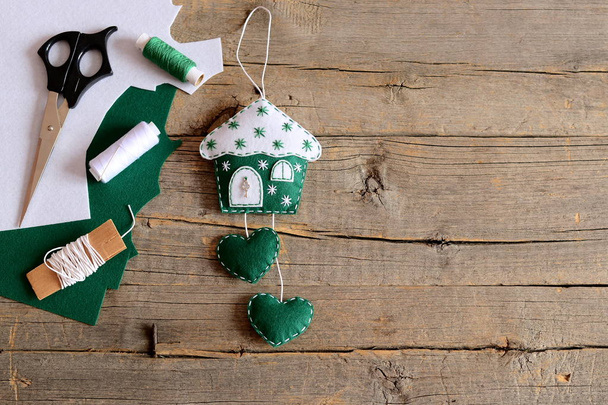 雪片と金属製の鍵で飾られた緑の感じの家。心とクリスマスのおもちゃの家,はさみ,糸,テキストのためのコピースペースと古い素朴な木の背景にシートを感じました.美しい壁の装飾。クリスマスホームの装飾。トップ表示  - 写真・画像