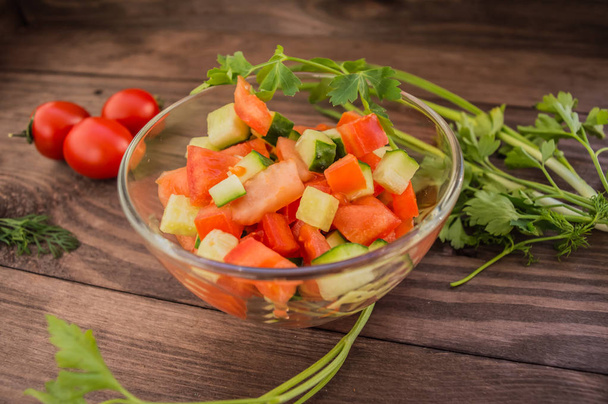 frischer Salat mit Tomaten und Gurken auf Holzuntergrund in transparentem Teller. - Foto, Bild