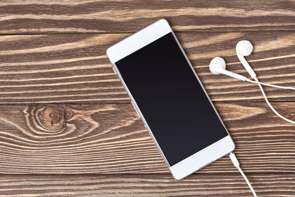 Smartphone e fones de ouvido em fundo de madeira
 - Foto, Imagem