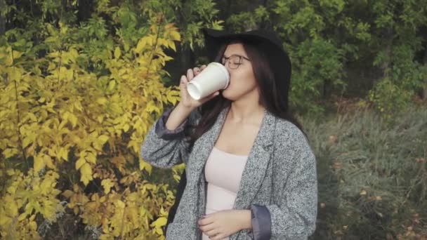 Young pretty woman in black hat and glasses drinking coffee outdoor - Metraje, vídeo