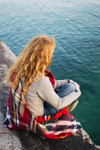 Young woman with red hair curls sitting in a scarf at the seacoast - Foto, Imagen