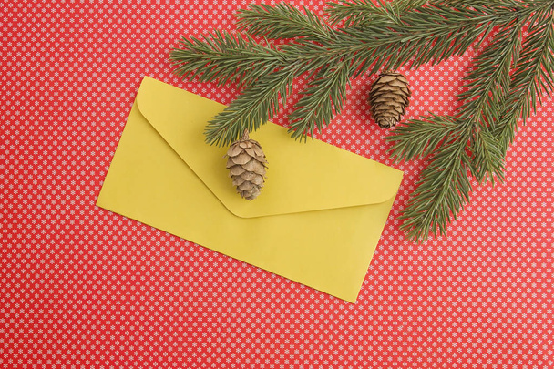 Christmas composition with fir tree branch, cones and yellow envelope on red background. Top view, flat lay. Copy space for text - Photo, Image
