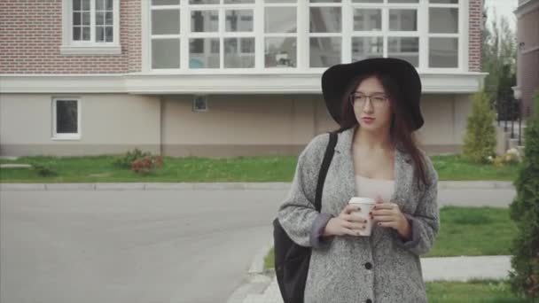 Bella donna in cappello nero e occhiali con tazza di caffè che cammina per la strada
 - Filmati, video