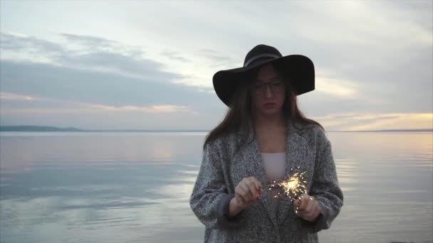 Αρκετά ευτυχισμένη γυναίκα φώτα βεγγαλικά στην ακτή της θάλασσας στο ηλιοβασίλεμα - Πλάνα, βίντεο