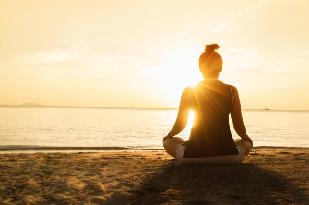 sylwetka młoda kobieta praktykowania jogi na plaży o zachodzie słońca. - Zdjęcie, obraz