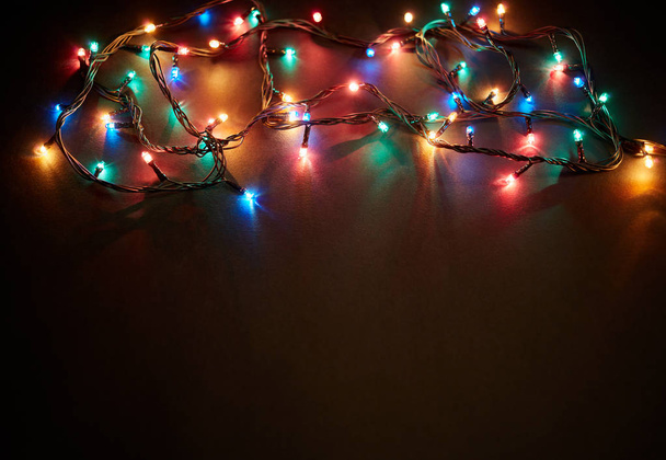 Karácsonyi háttér fények és szabad szöveges hely. Karácsonyi fények határán. Világító színes karácsonyi fények fekete háttér. Újév. Karácsonykor. Dekoráció. Fűzér. - Fotó, kép