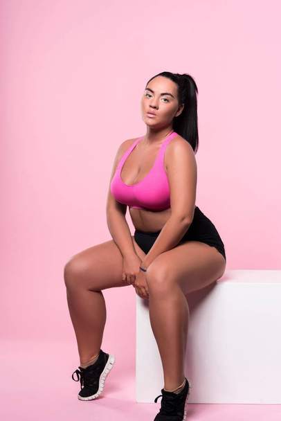 Sexy plump mulatto woman sitting on pink background - Foto, Imagem