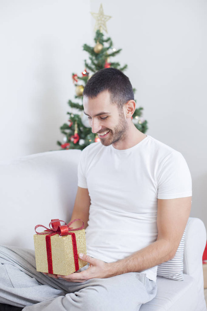 man on the sofa holding a Christmas present - Фото, изображение