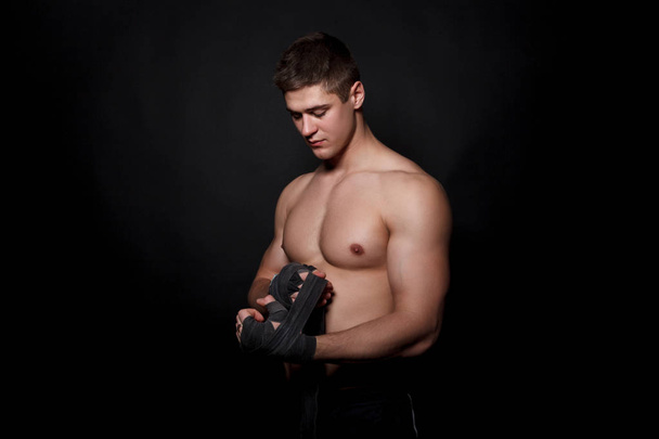 Спортивный боксер тянет за запястье. Кавказская модель мужчины изолирована на тёмном фоне
. - Фото, изображение