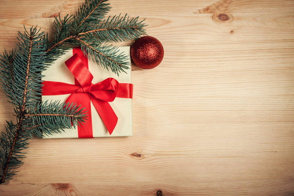 De gift van Kerstmis verpakt in rood lint met spar takje op houten achtergrond - Foto, afbeelding