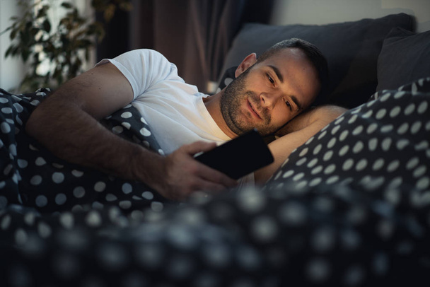 jovem viciado homem acordado na cama usando smartphone
 - Foto, Imagem