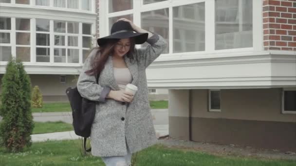 黒い帽子と通りを歩いてコーヒーのカップとグラスのきれいな女性 - 映像、動画