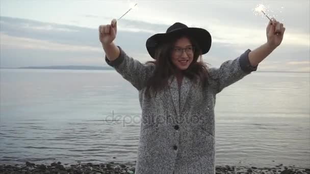 Όμορφη γυναίκα άλματα και πανηγυρισμούς με βεγγαλικά στην ακτή της θάλασσας στο ηλιοβασίλεμα - Πλάνα, βίντεο