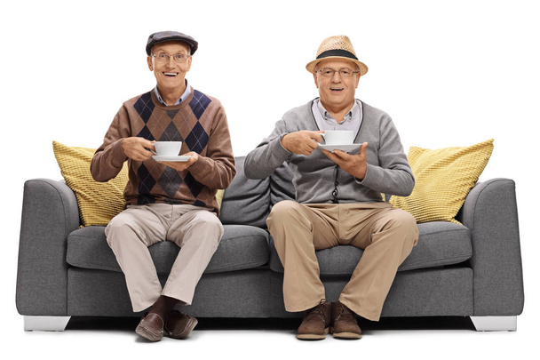 Joyful seniors with cups sitting on a sofa - Фото, зображення