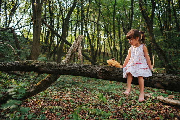 little girl playing with her bear in the woods. girl sitting on  - Photo, Image