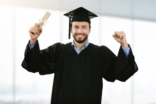 cheerful smiling graduate wearing gown at graduation ceremony - Photo, Image