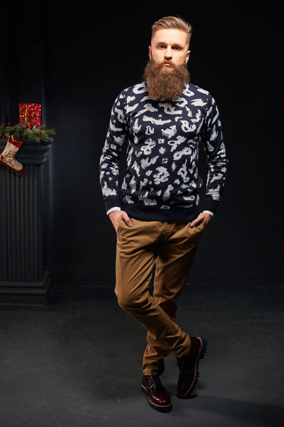 Beautiful bearded man in dark studio with christmas sock on background - Zdjęcie, obraz