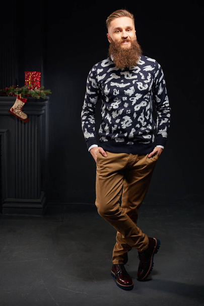 Attractive smiling man with beard in dark studio with christmas sock on background - Fotoğraf, Görsel