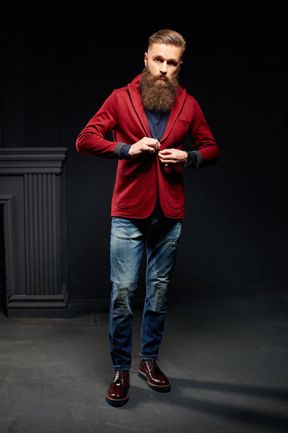 Attractive man with long beard in dark studio wearing red jacket - Foto, imagen