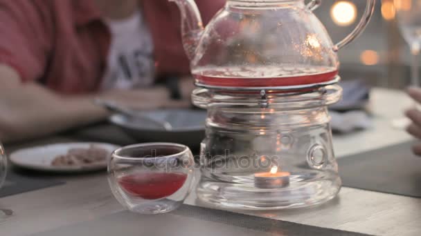 Transparent teapot heated candle in a cafe, people at the table - Footage, Video