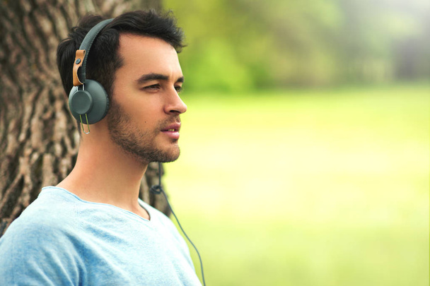 Portrait of beautiful dreaming young man with headphones, listen music on the tree background. - Фото, зображення