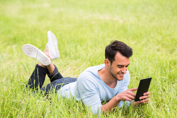 Happy business man smiling and lying on the green grass with his device. - Фото, изображение