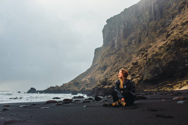 Woman sitting on seashore with black sand - Foto, Imagen