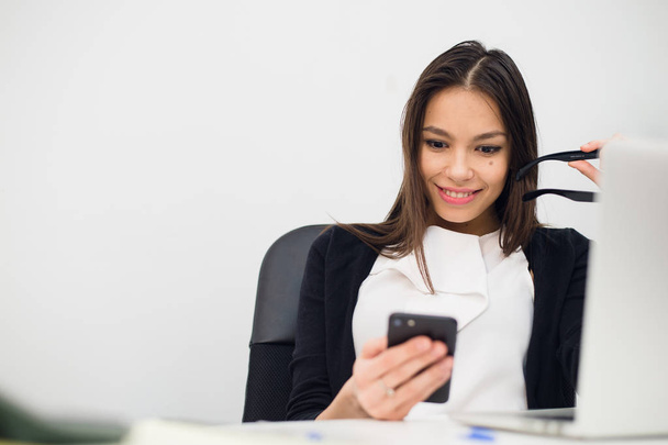 Empresária entusiasmada ganhando após a realização ler telefone inteligente sentado em um desktop no escritório
 - Foto, Imagem