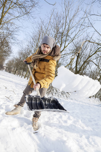 young man shoveling snow near a small wood - Fotó, kép