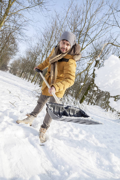 young man shoveling snow near a small wood - Фото, зображення