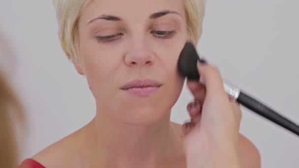 クローズ アップ ショット。プロのメークアップ アーティストの女性の顔におしろいを塗り - 映像、動画
