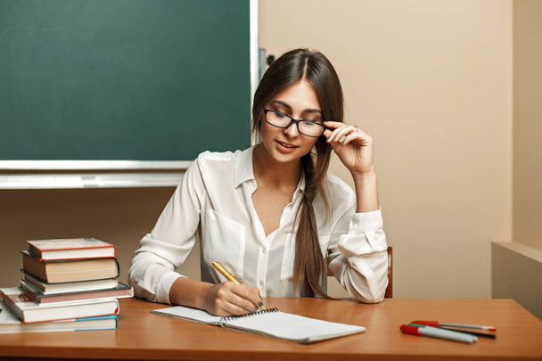 Όμορφη νεαρή γυναίκα με τα γυαλιά να σπουδάσουν στο Πανεπιστήμιο, διαβάζοντας βιβλία και γράφει σε ένα σημειωματάριο. - Φωτογραφία, εικόνα