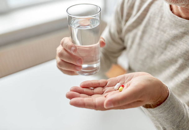 close up of old man hands with pills and water - Foto, Imagen