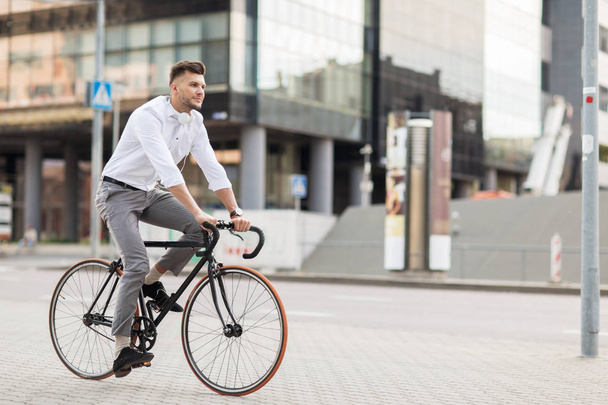 man with headphones riding bicycle on city street - Zdjęcie, obraz