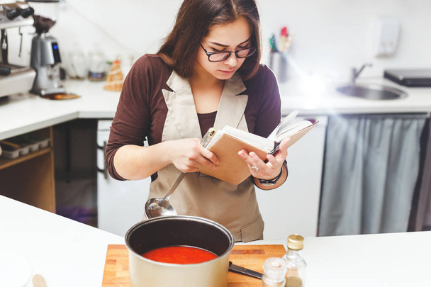Κορίτσι Προετοιμασία ντομάτα σούπα συνταγές σύμφωνα με το βιβλίο. - Φωτογραφία, εικόνα