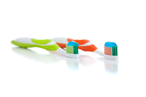Green and orange toothbrushes on a white background - Fotoğraf, Görsel