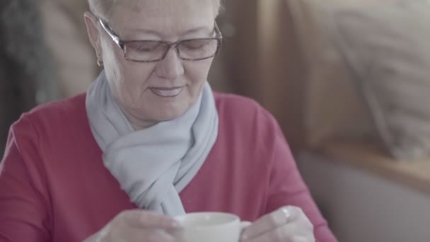 Mature woman in a red sweater and a purple scarf drinking tea - Imágenes, Vídeo