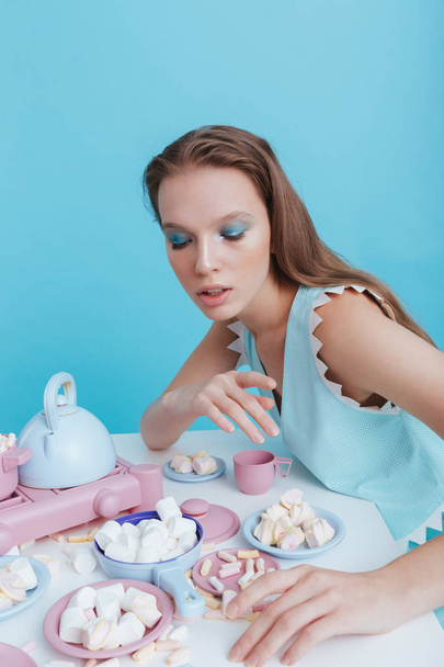 Attractive young woman sitting and eating marshmallows with plasic dishes - Foto, Bild